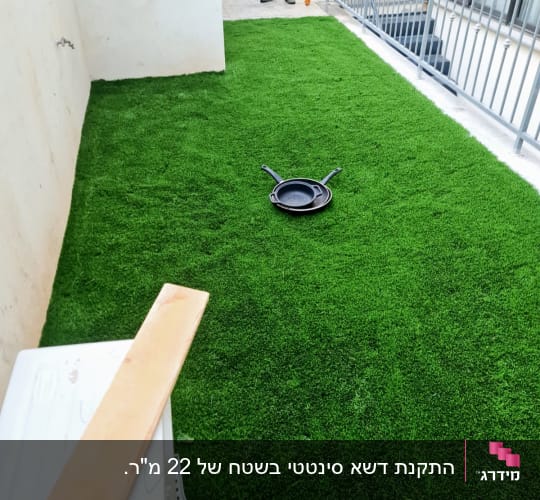משטח דשא סינטטי מותקן בחצר היקפית לצד מעקה מתכת